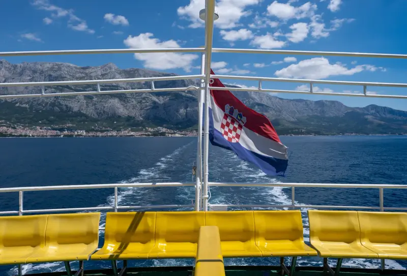 Bandera de Croacia ondeando en un ferry con la localidad de Makarska al fondo.