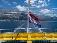 Bandera de Croacia ondeando en un ferry con la localidad de Makarska al fondo.