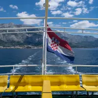 Bandera de Croacia ondeando en un ferry con la localidad de Makarska al fondo.